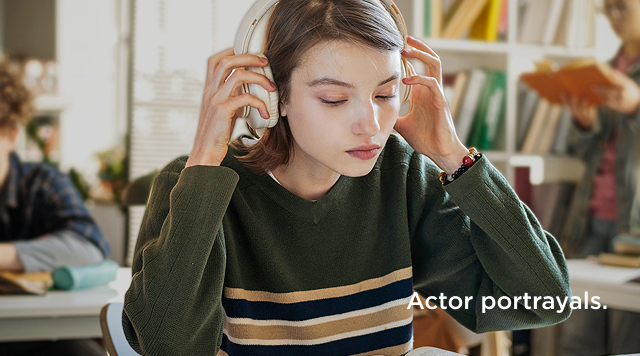 Teenage girl with headphones studying at a desk in a well-lit room.