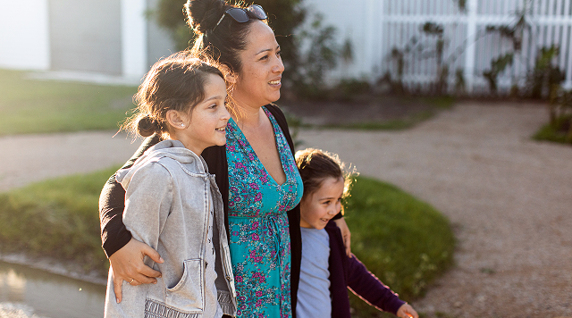 A woman and her two daughters stand outside, smiling.