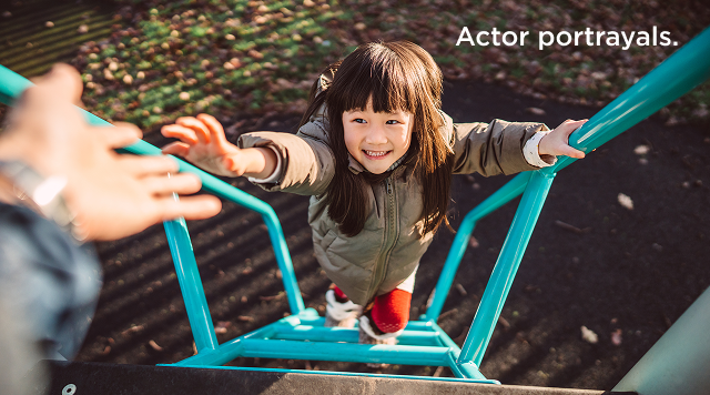 A young girl smiles and reaches for an adult's hand while climbing a playground ladder.